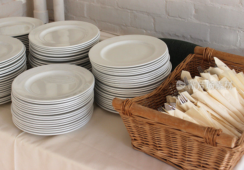 自助餐上成堆的白色盘子、餐具(刀/叉/餐巾)